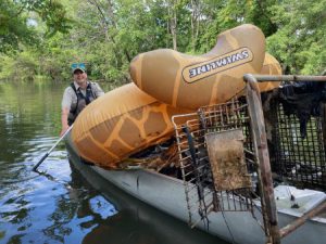 Woman in boat with trash collected from water, including an inflatable raft. Photo courtesy of Ecorse Creek Committee.